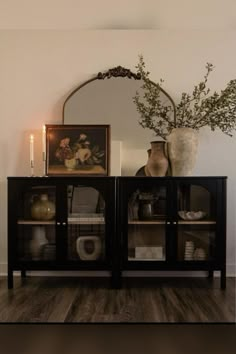 a vase with some flowers on top of it next to a glass doored cabinet