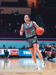 a female basketball player is running with the ball in her hand and people watching from the stands