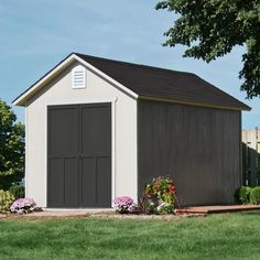 a storage shed in the middle of a grassy area with flowers around it and trees