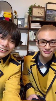 two young men sitting next to each other wearing yellow uniforms and black rimmed glasses