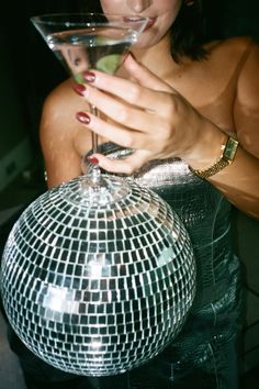 a woman holding a martini glass in her right hand and looking at the mirror ball