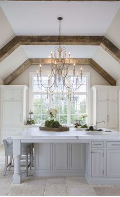 a large kitchen with an island and chandelier in the center, surrounded by white cabinets