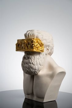 a white bust with a gold ring on it's head, sitting on a table