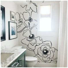 a bathroom with black and white flowers painted on the wall next to the shower curtain