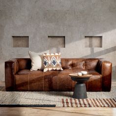 a brown leather couch sitting on top of a wooden floor next to a table and chair