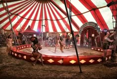 two women are dancing in front of a circus tent while others watch from the sidelines