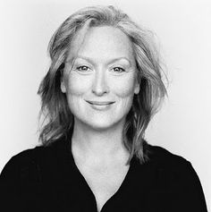 a black and white photo of a woman with blonde hair smiling at the camera while wearing a black shirt