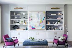 a living room with two chairs and a coffee table in front of the bookshelves