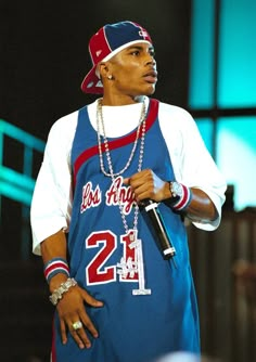 a man in a blue jersey holding a microphone and wearing a chain around his neck