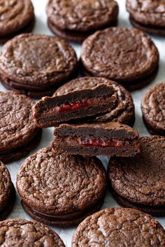 chocolate cookies with raspberry filling are arranged on a sheet of parchment paper and ready to be eaten