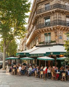 many people are sitting at tables under umbrellas on the sidewalk in front of a building