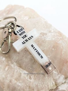 a cross keychain that says i am with you always on it sitting on top of a rock