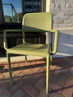 a green plastic chair sitting on top of a brick sidewalk next to a building with a window