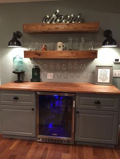 a wine cooler in the middle of a kitchen with shelves above it and glasses on top