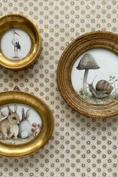 three framed pictures of rabbits and mushrooms in gold frames on a white tablecloth with an embellished mushroom