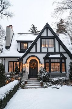 a white house with black trim and windows in the snow covered front yard is lit up by christmas lights