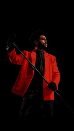 a man in a red jacket and black shirt holding a microphone with his right hand