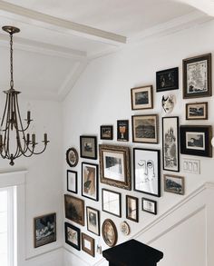 a staircase with many framed pictures on the wall and a chandelier hanging from the ceiling