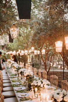 a long table is set with white flowers and candles for an outdoor wedding reception in the woods