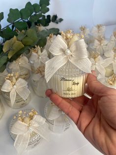 a hand holding a small glass bottle with a bow on it next to some flowers