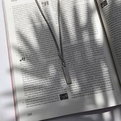 an open book with a necklace on it sitting next to a tree branch and shadow