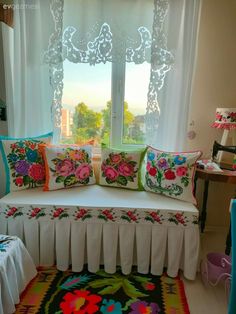 a white couch sitting in front of a window covered in pillows and colorful rugs