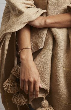 a woman is holding a bag with tassels in her hands and wearing a tan coat