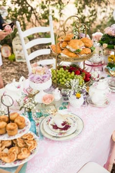 a table topped with plates and cups filled with food next to a cake stand full of pastries