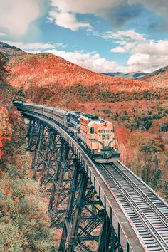 a train traveling over a bridge in the middle of trees and hills with fall colors