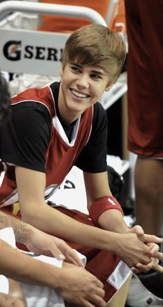 a young man sitting on top of a basketball court next to another person holding his hand out