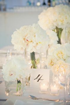 white flowers are in vases with candles and place cards on the tables at this wedding reception