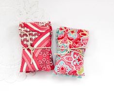 two small notebooks wrapped in red and blue fabric with white lace on them, sitting next to each other