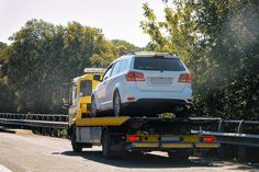 a white car is on the back of a yellow tow truck with trees in the background