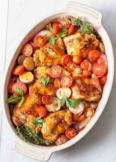 chicken and tomatoes in a white casserole dish with fresh herbs on the side