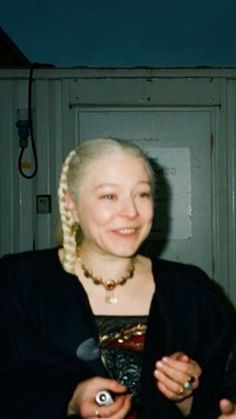 a woman with blonde hair is smiling and holding something in her hands while standing next to a door