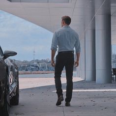 a man walking past a parked car in front of a tall white building with columns