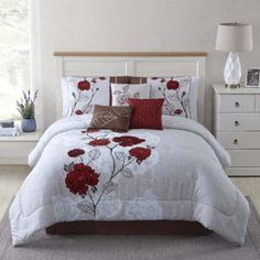 a white bed with red flowers on it in a bedroom next to a night stand