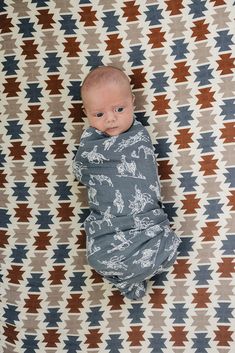 a baby wrapped in a blanket laying on top of a patterned wallpaper covered floor