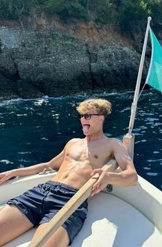 a shirtless man on a boat in the water with his tongue out and sunglasses on