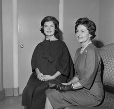 two women sitting next to each other on a couch in front of a wall and door