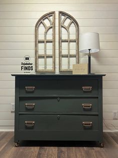 a dresser with two mirrors on top and a lamp next to it in front of a white wall