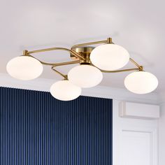 a ceiling light with five white globes hanging from it's golden metal fixture