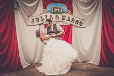 a bride and groom are dancing in front of a red stage with white drapes