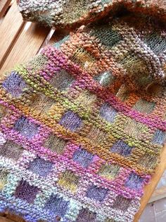 a multicolored knitted blanket sitting on top of a wooden floor next to a window