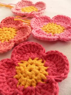 four crocheted flowers sitting on top of a white table next to each other