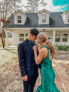 a man and woman standing in front of a house wearing formal wear, looking at each other