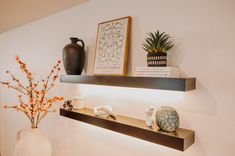 two shelves with vases and other decorative items on them in a white walled room