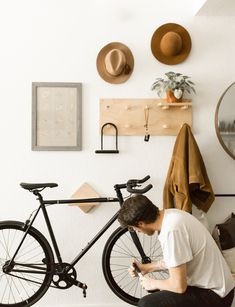 a man sitting on the ground next to a bike in front of a wall with hats