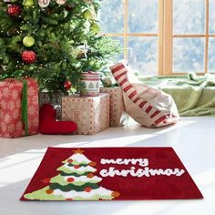 a christmas tree with presents under it in front of a window and a red rug on the floor