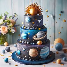 a three tiered cake with planets and stars on the top, surrounded by flowers